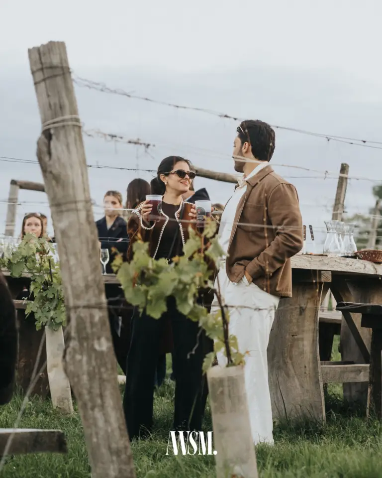 Gäste mit Rotwein in Bechern plaudern an einem Holztisch zwischen den Rebstöcken unter bewölktem Himmel – Vineyard Edition, 24.05.2025