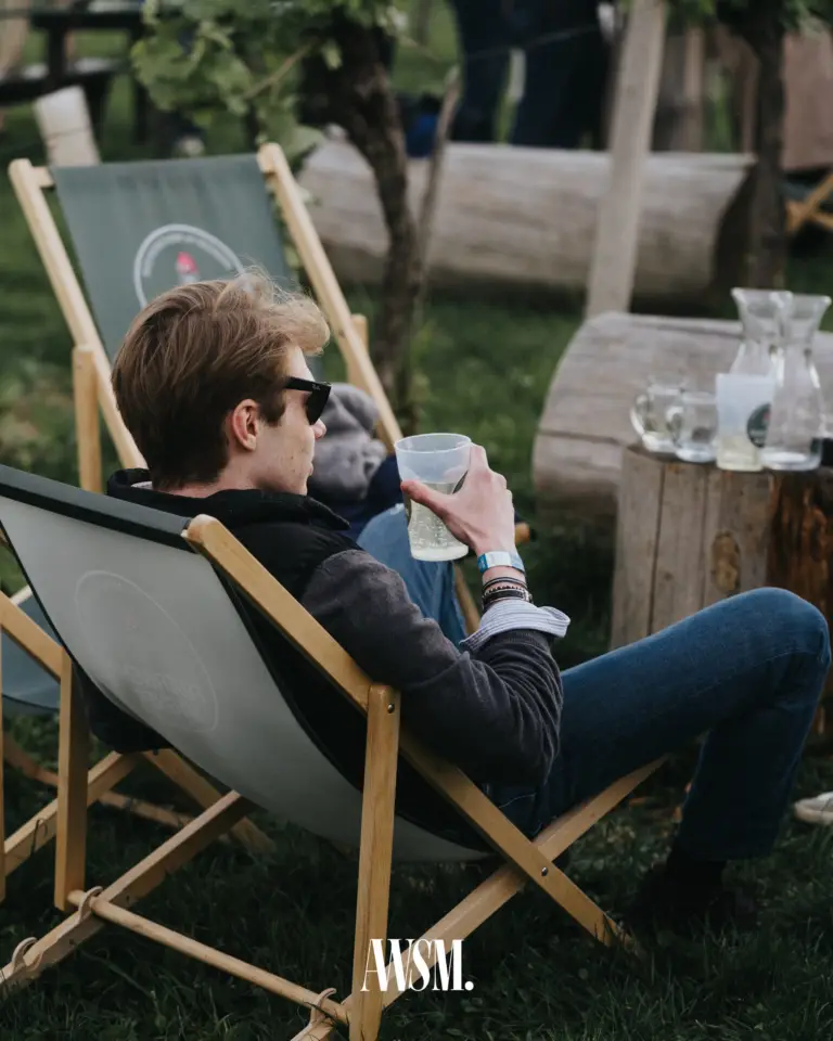 Gast mit Sonnenbrille lehnt im Liegestuhl mit Becher, daneben ein Baumstumpftisch mit Karaffen – Vineyard Edition, 24.05.2025