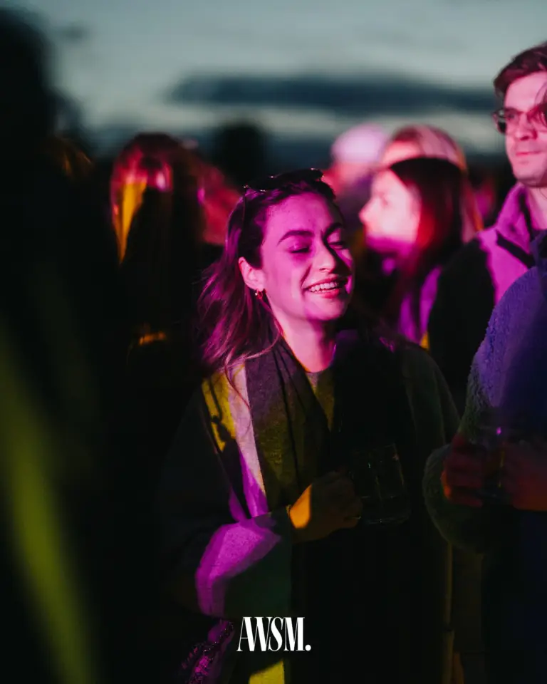 Lächelnder Gast mit Glaskrug im violetten und gelben Partylicht, umgeben von der Menge in der Dämmerung – Vineyard Edition, 24.05.2025