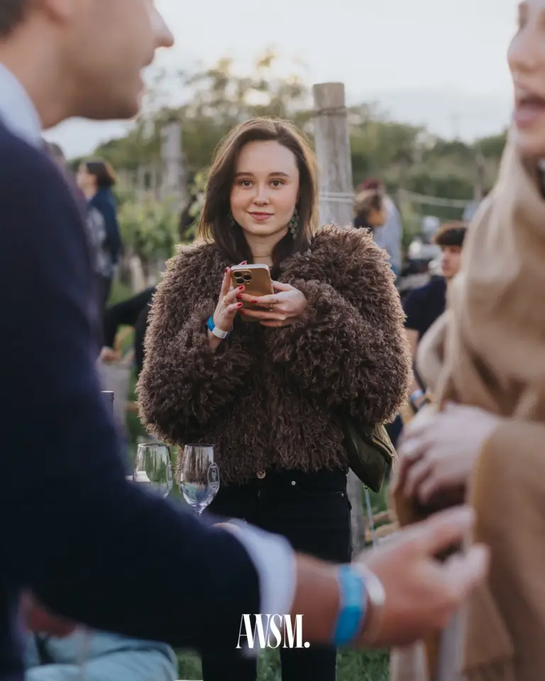 Lächelnder Gast in brauner Plüschjacke mit Handy zwischen anderen Gästen im Weinberg am Nussberg – Vineyard Edition, 24.05.2025