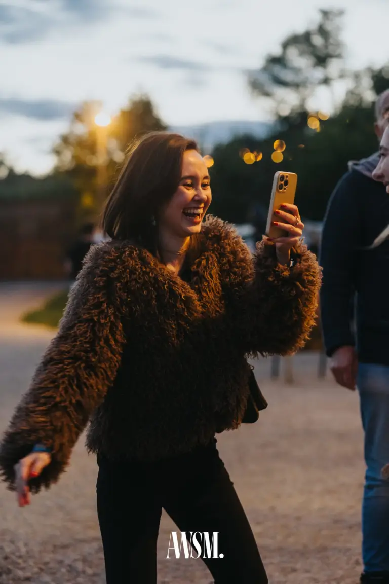 Lachender Gast in brauner Plüschjacke tanzt mit dem Handy in der Hand, dahinter Lichter in der Dämmerung – Vineyard Edition, 24.05.2025