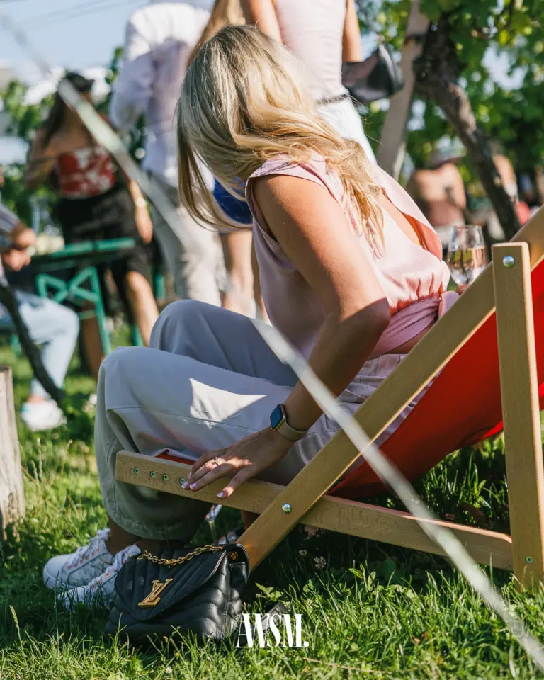 Gast in rosa Top sitzt im roten Liegestuhl auf der Wiese, daneben Weinglas, im Hintergrund Gäste im Weinberg – Vineyard Edition, 19.07.2025