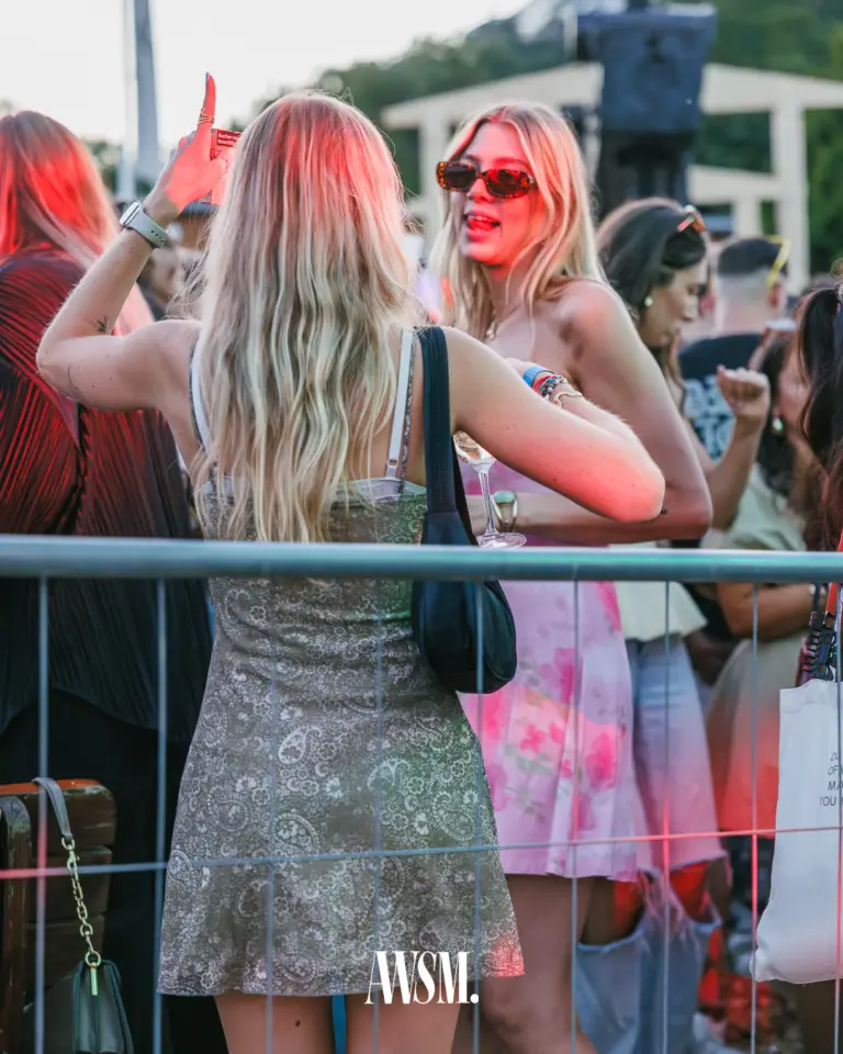 Guests celebrating at the barrier by the DJ area, one in red sunglasses holding a wine glass, under red spotlight – Vineyard Edition, 19 July 2025