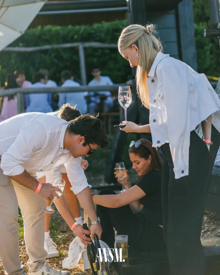 Mann schenkt aus einer Flasche nach, daneben eine Frau in weißer Jacke mit Sektglas und eine sitzende Frau – Vineyard Edition, 14.06.2025