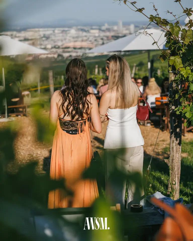Zwei Frauen von hinten blicken über den Weinberg und die Sonnenschirme auf das weite Stadtpanorama – Vineyard Edition, 14.06.2025