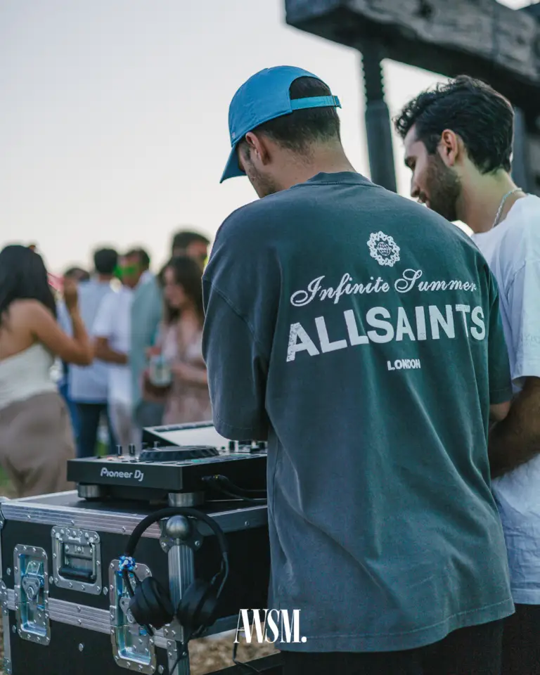 DJ mit Kappe von hinten am DJ-Pult, Kopfhörer am Case, dahinter Gäste im Weinberg am Nussberg im Abendlicht – Vineyard Edition, 14.06.2025
