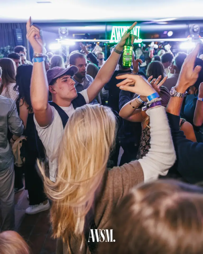 Guests dancing with arms raised and a bottle in hand in front of a green AWSM neon sign – Vineyard Edition, 13 September 2025