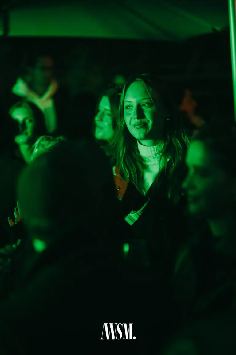 Lächelnder Gast mit Rollkragen zwischen weiteren Gästen in grünem Licht unter dem Schirm – Vineyard Edition, 04.10.2025