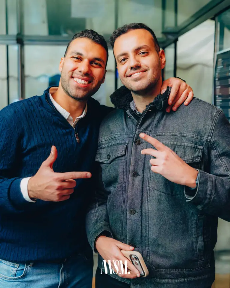 Zwei Gäste Arm in Arm lachen in die Kamera und zeigen mit den Fingern, dahinter eine Glasfront – NYE Skyline Edition, 31.12.2025