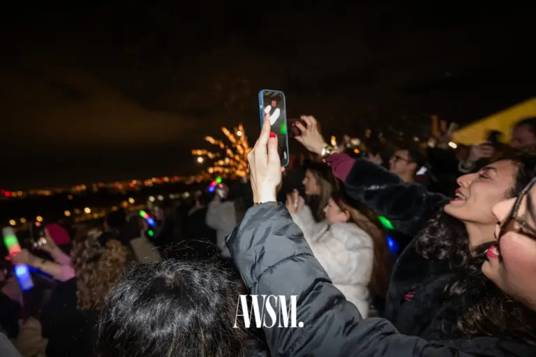 Gäste filmen draußen mit dem Handy das Feuerwerk über den Lichtern der Stadt, dazwischen bunte Leuchtstäbe – NYE Skyline Edition, 31.12.2025