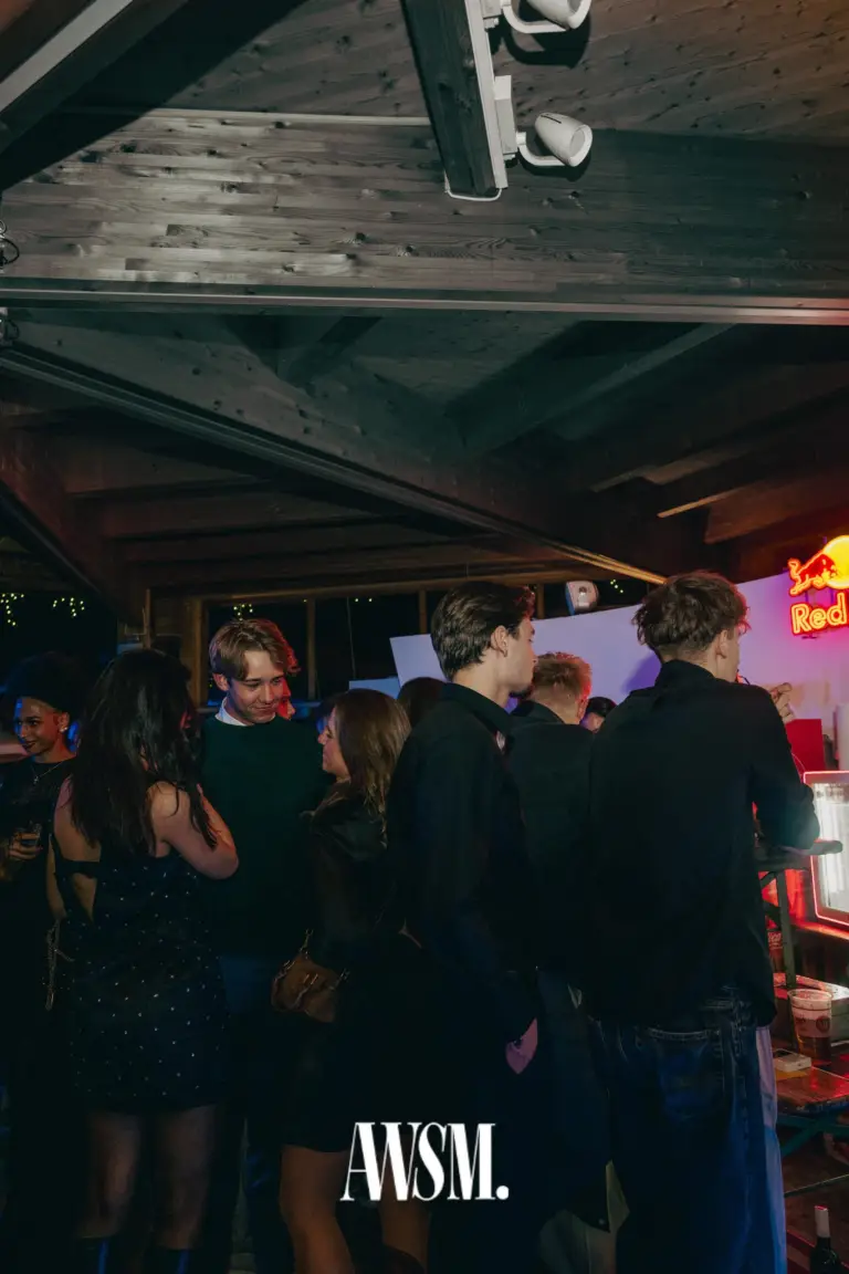 Gäste stehen in Gruppen unter der Holzdecke nahe der Bar, seitlich eine leuchtende Neonreklame – NYE Skyline Edition, 31.12.2025