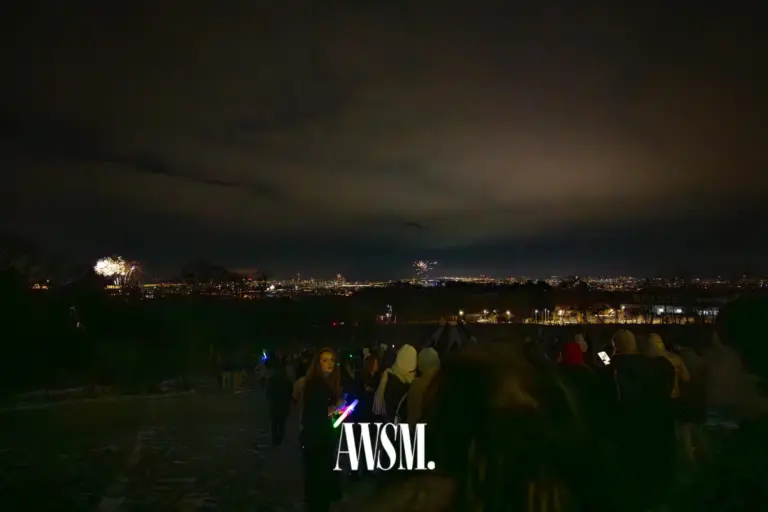 Gäste stehen nachts am Hang mit Blick über die Lichter der Stadt, in der Ferne leuchtet Feuerwerk – NYE Skyline Edition, 31.12.2025