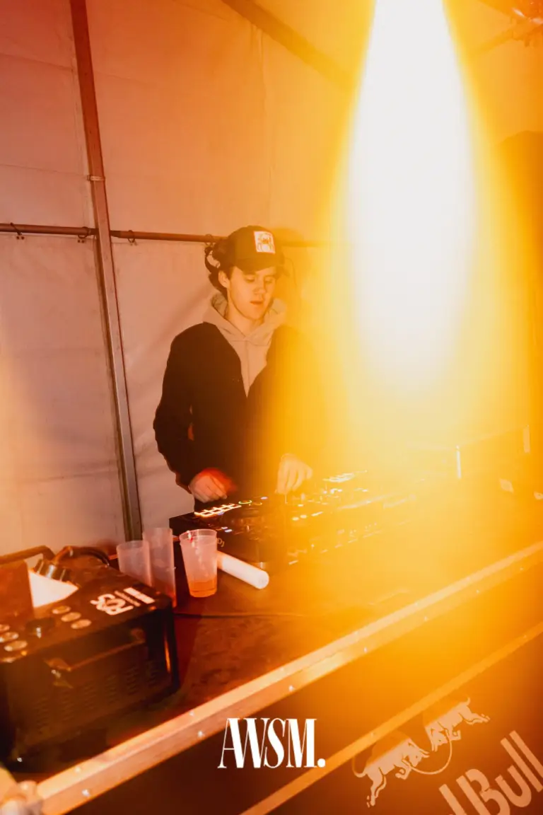 DJ mit Kappe und Kapuzenpulli legt im Zelt am Pult auf, daneben Becher und ein oranger Lichtschein – NYE Skyline Edition, 31.12.2025