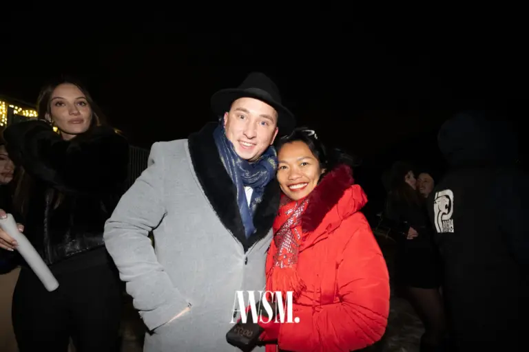 Zwei Gäste posieren nachts draußen, einer mit Hut und grauem Mantel, einer in roter Jacke mit Schal – NYE Skyline Edition, 31.12.2025