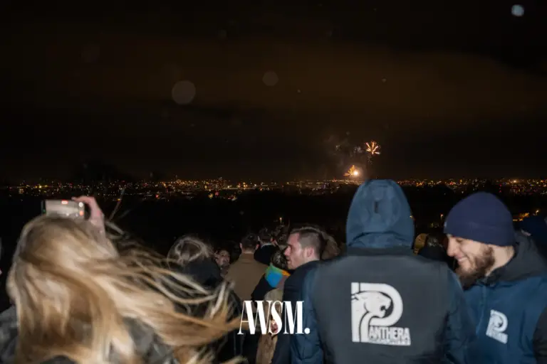 Gäste stehen nachts am Hang und blicken auf das Feuerwerk über den Lichtern der Stadt, einer filmt mit dem Handy – NYE Skyline Edition, 31.12.2025