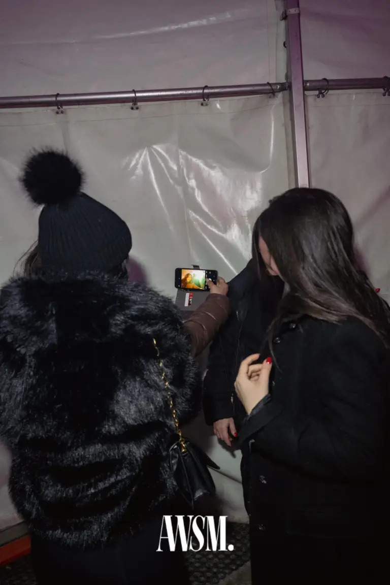 Gäste stehen vor der weißen Zeltwand, einer mit Bommelmütze und Plüschjacke, einer fotografiert mit dem Handy – NYE Skyline Edition, 31.12.2025