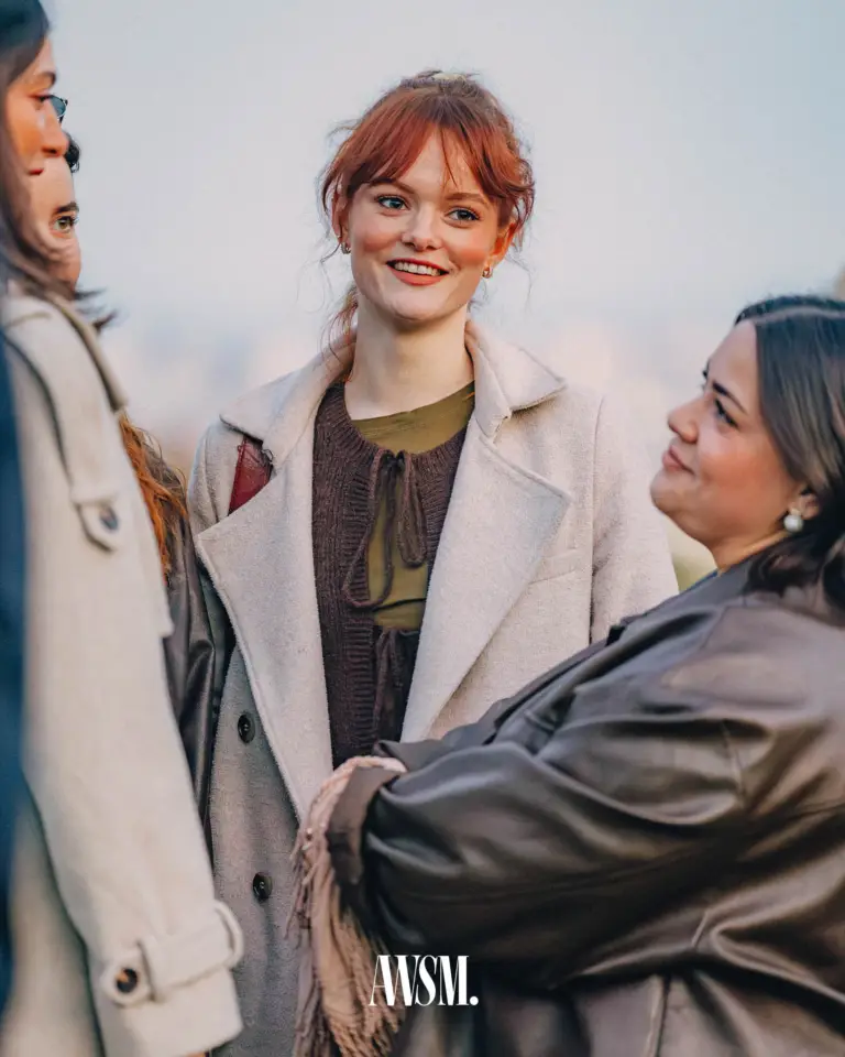 Frau mit roten Haaren im hellen Mantel lächelt im Kreis von Gästen im Freien am Reisenberg – Grand Vineyard Opening, 11.04.2026