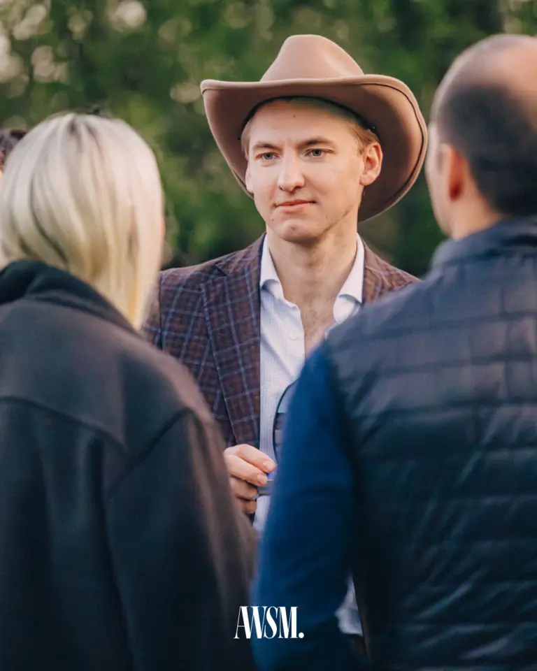 Mann mit Cowboyhut und kariertem Sakko im Gespräch mit Gästen im Freien, dahinter Bäume – Grand Vineyard Opening, 11.04.2026