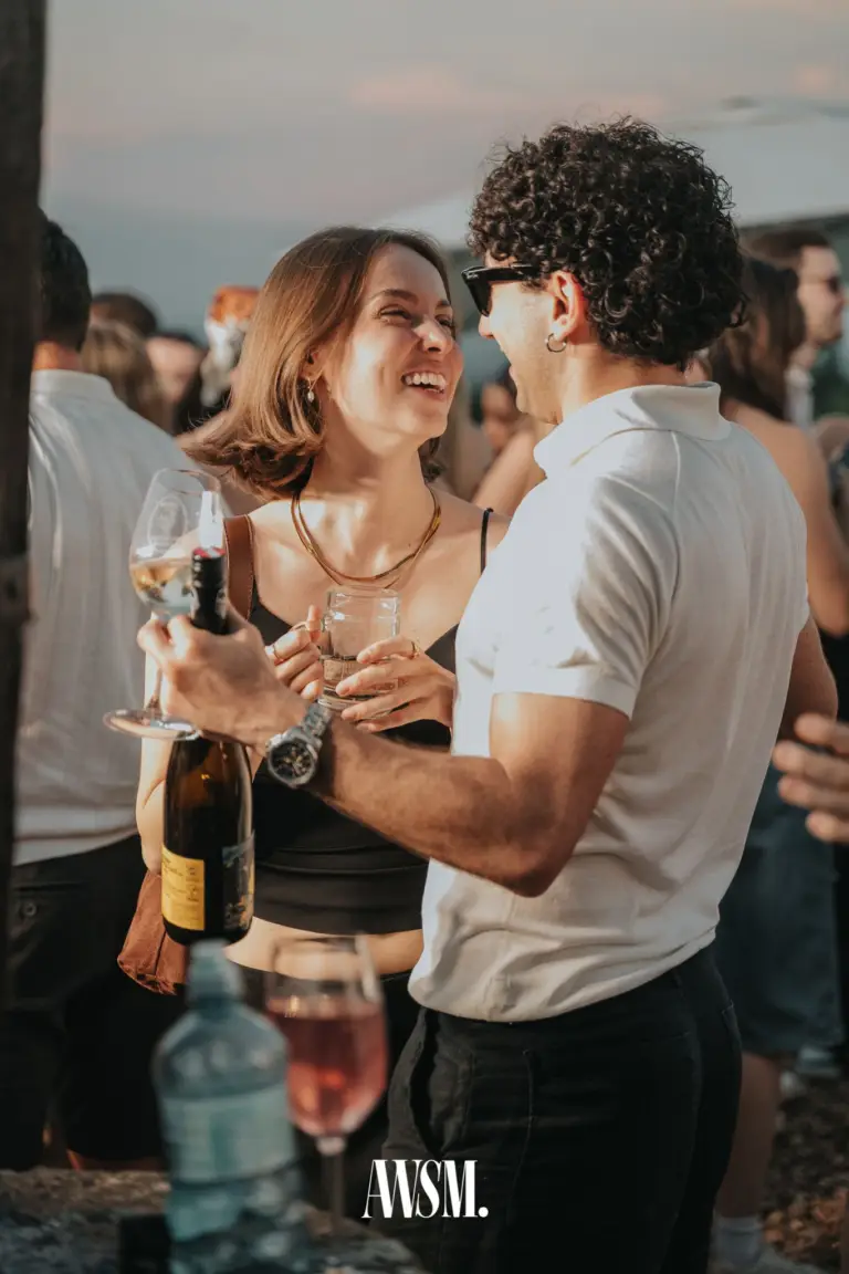 Lachende Frau mit Glas im Gespräch mit Gast mit Weinflasche und Weinglas im Abendlicht – Vineyard Summer Opening, 20.06.2026