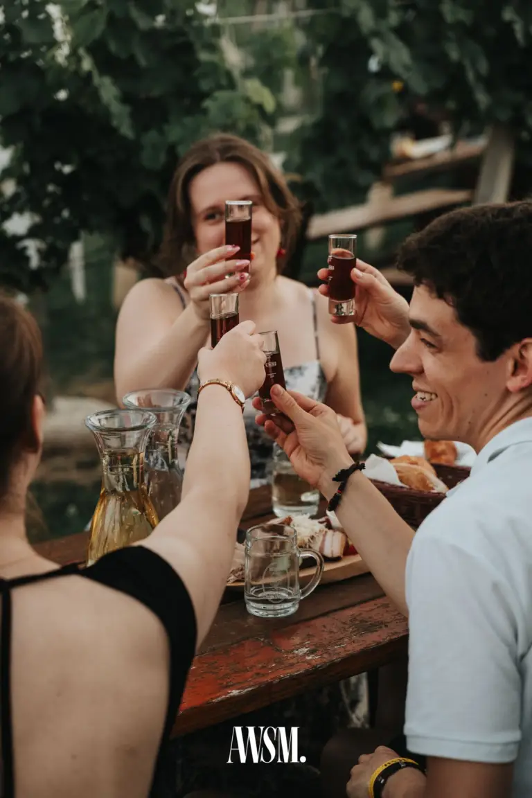 Guests toasting with shot glasses at a wooden table with carafes and snacks beneath the vines on Nussberg – Vineyard Summer Opening, 20 June 2026