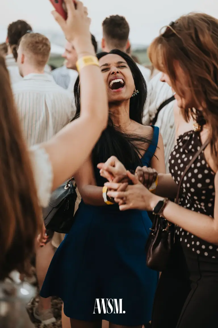 Woman in a blue dress laughing out loud, holding hands with a woman in a polka-dot top in the crowd on Nussberg – 20 June 2026