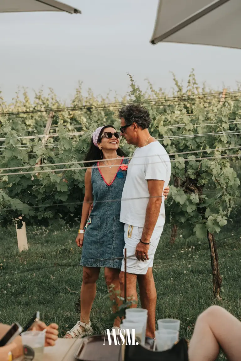 Paar steht Arm in Arm vor grünen Rebzeilen unter weißen Schirmen, vorne Becher auf dem Tisch am Nussberg – Vineyard Summer Opening, 20.06.2026