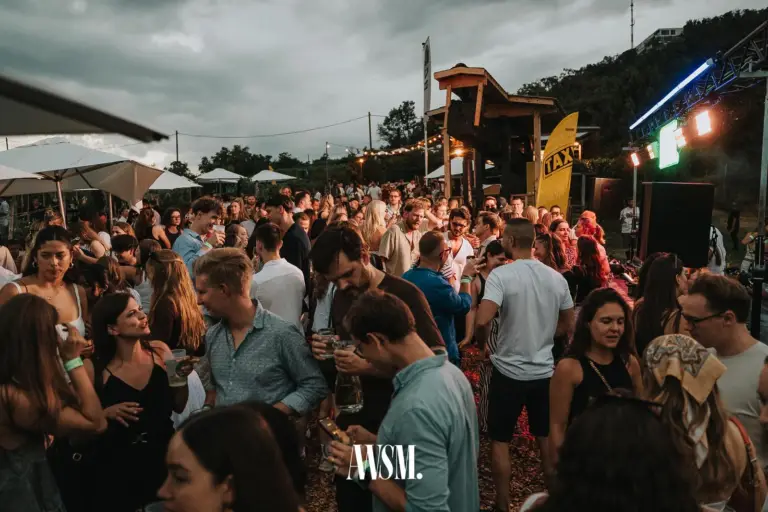 Busy grounds on the Nussberg at dusk, with parasols, string lights, a wooden tower and the stage on the right – Vineyard Summer Edition, 18 July 2026