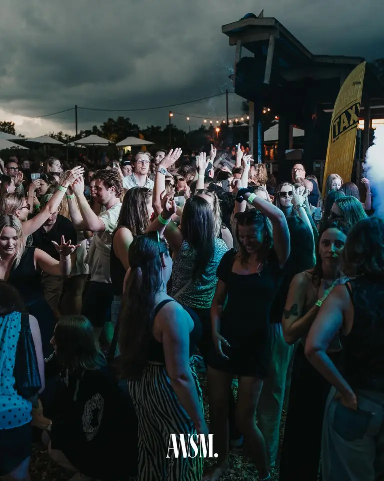 Guests dance with raised hands in front of the wooden tower, dark clouds, string lights and parasols above them – Vineyard Summer, 18 July 2026