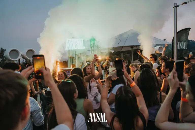 Gäste halten in der Dämmerung Handys und Becher hoch, dahinter Nebelfontänen und die AWSM-Leuchtschrift am DJ-Pult – Skyline Edition, 08.08.2026