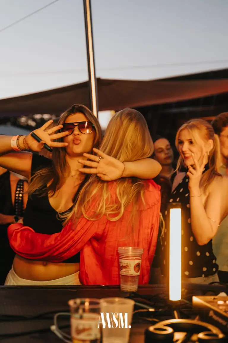 Frau mit Sonnenbrille macht einen Kussmund und umarmt eine Frau in roter Bluse am DJ-Pult, daneben lachende Gäste – Skyline Edition, 08.08.2026