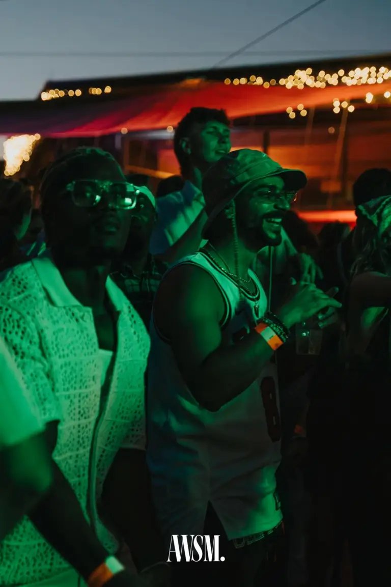 Mann mit Fischerhut und Tanktop lacht im grünen Licht, neben ihm ein Gast mit Brille, dahinter Lichterketten – Skyline Edition, 08.08.2026