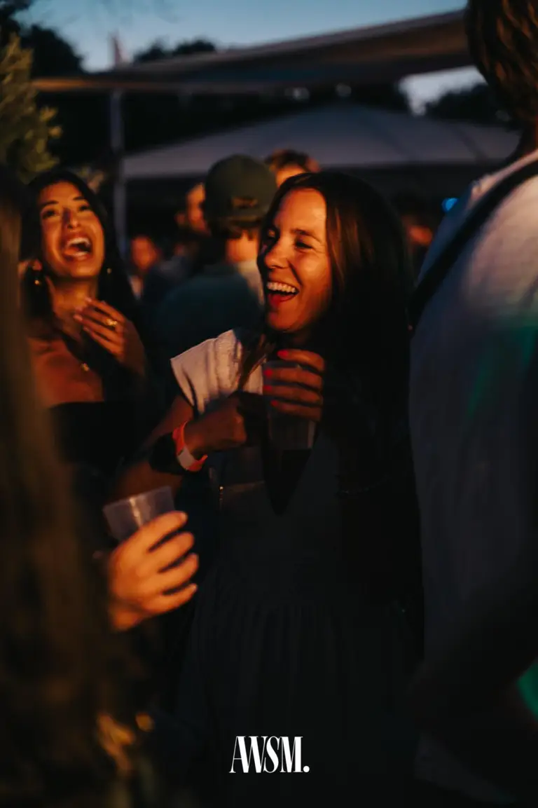 Zwei Frauen lachen herzhaft mit Bechern in der Hand, hinter ihnen weitere Gäste und ein Schirm im Abendlicht – Skyline Edition, 08.08.2026