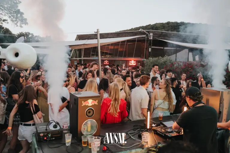 DJ mit Kappe legt vor voller Terrasse auf, Nebelfontänen, dahinter ein Pavillon mit Glasfront und ein bewaldeter Hügel – Skyline Edition, 08.08.2026