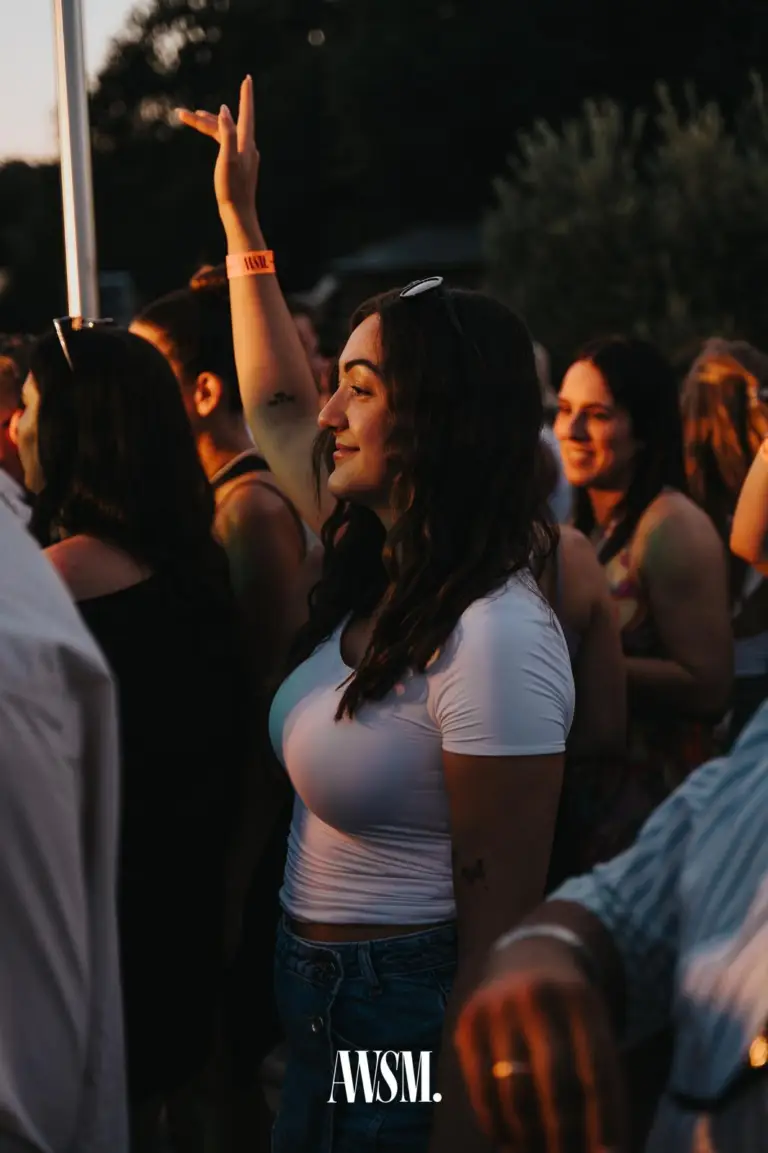 Frau im weißen T-Shirt hebt lächelnd eine Hand, rundum Gäste im goldenen Abendlicht vor Olivenbäumen – Skyline Edition, 08.08.2026