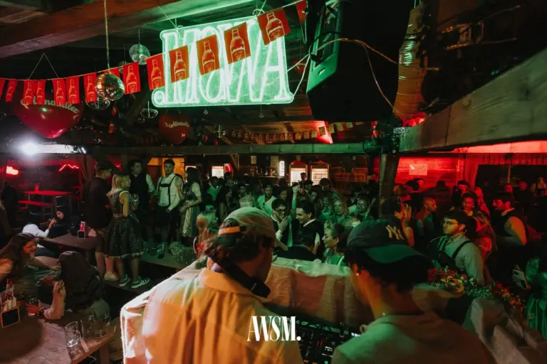 Blick über das DJ-Pult auf die volle Tanzfläche mit Gästen in Tracht, darüber Wimpelgirlande und Leuchtschrift – AWSM. GOES KAISER WIESN, 27.09.2026