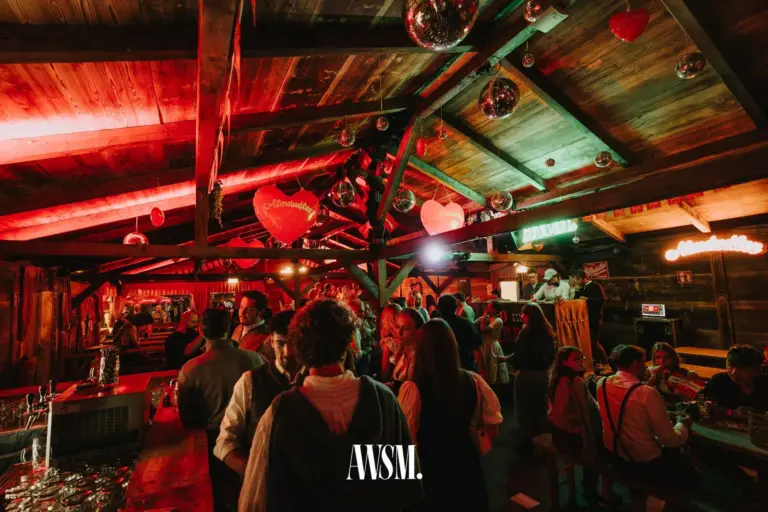 Rot beleuchtetes Holzdach mit Herzen und Discokugeln über feiernden Gästen, links die Bar – AWSM. GOES KAISER WIESN, 27.09.2026