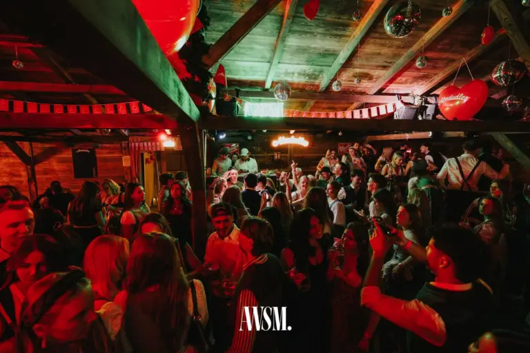 Volle Tanzfläche unter dem Holzdach, Gäste heben die Hände, darüber Herzballons, Wimpel und Discokugeln – AWSM. GOES KAISER WIESN, 27.09.2026