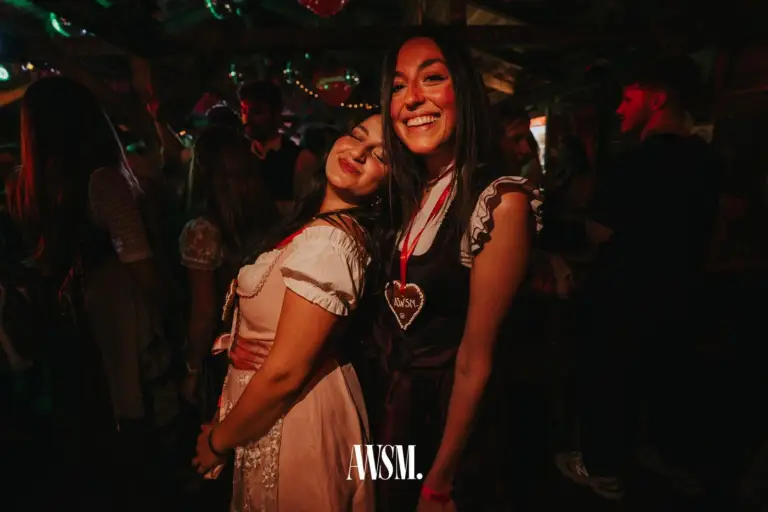 Zwei Frauen im Dirndl posieren Wange an Wange, eine trägt ein Lebkuchenherz um den Hals – AWSM. GOES KAISER WIESN, 27.09.2026